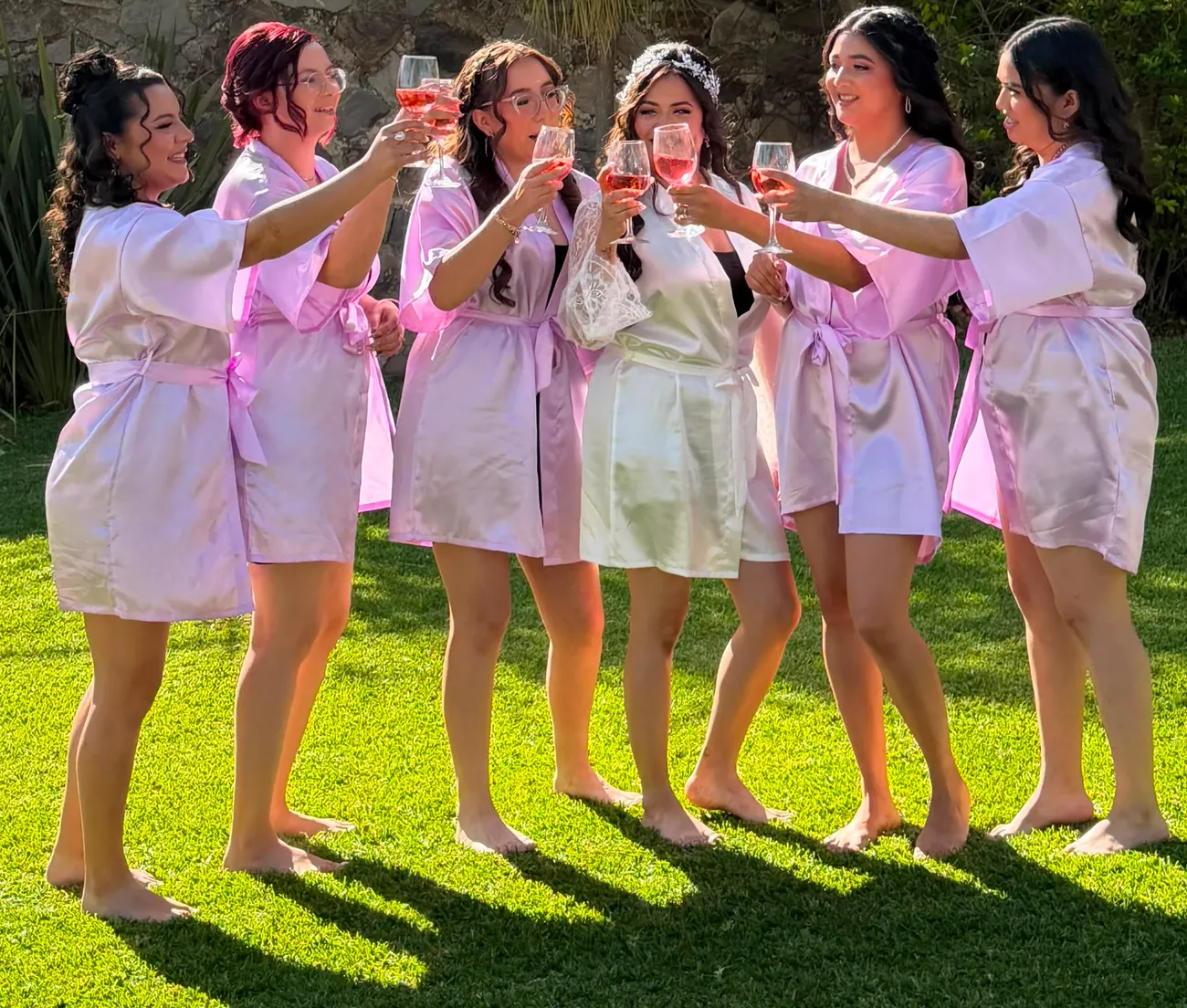 Novia brindando con sus damas en batas rosas en el jardín
